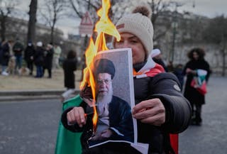 A protester holds a burning poster of Iran's Supreme Leader Ayatollah Ali Khamenei during a rally in Paris
